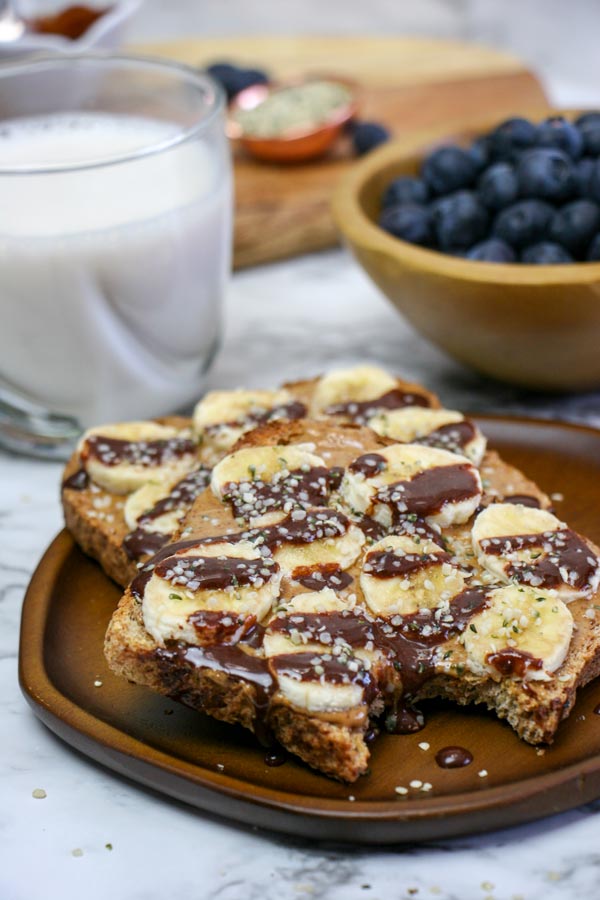 peanut butter chocolate banana breakfast toasts on a plate with a bite taken out of one, and a glass of milk behind it
