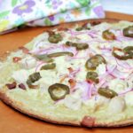 closeup of a whole jalapeno bacon chicken pizza on a pizza peel with a flower print napkin in the background