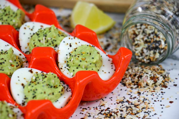 up close avocado everything bagel deviled eggs with jar of spicy everything bagel seasoning spilled