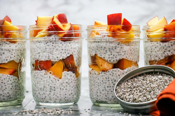 four jars filled with layered vanilla chia pudding and fresh peaches