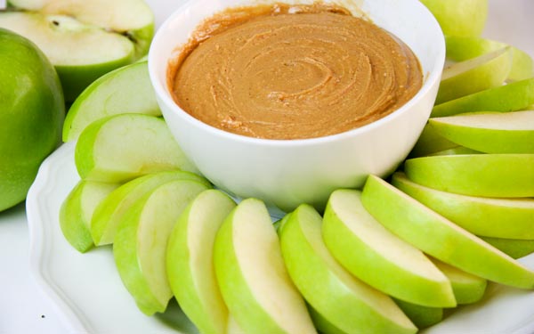 closer in view of mounded green apple slices and bowl of peanut butter honey apple dip healthy snack for kids
