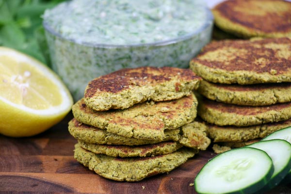 vegan spinach falafel stacked in front of diary free tzatziki sauce with cucumbers