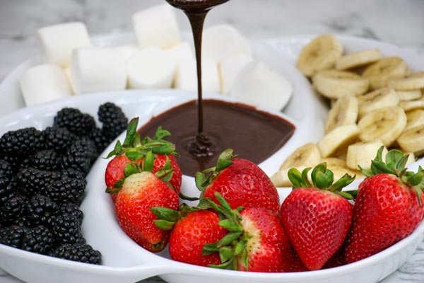 serving dish of blackberries, strawberries, banana slices, and marshmallows with pool of healthy vegan chocolate syrup (chocolate sauce) in center for dipping