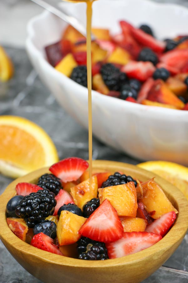 bowl of sweet spicy fruit salad with honey orange sriracha dressing being drizzled over it